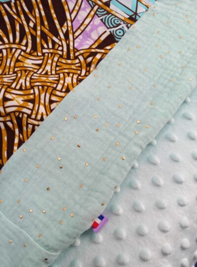 couverture plaid bébé patchwork wax motifs spirales bleu clair violet clair argenté et double gaze couleur bleu ciel/pastel à pois doré. Doublure en minky à pois